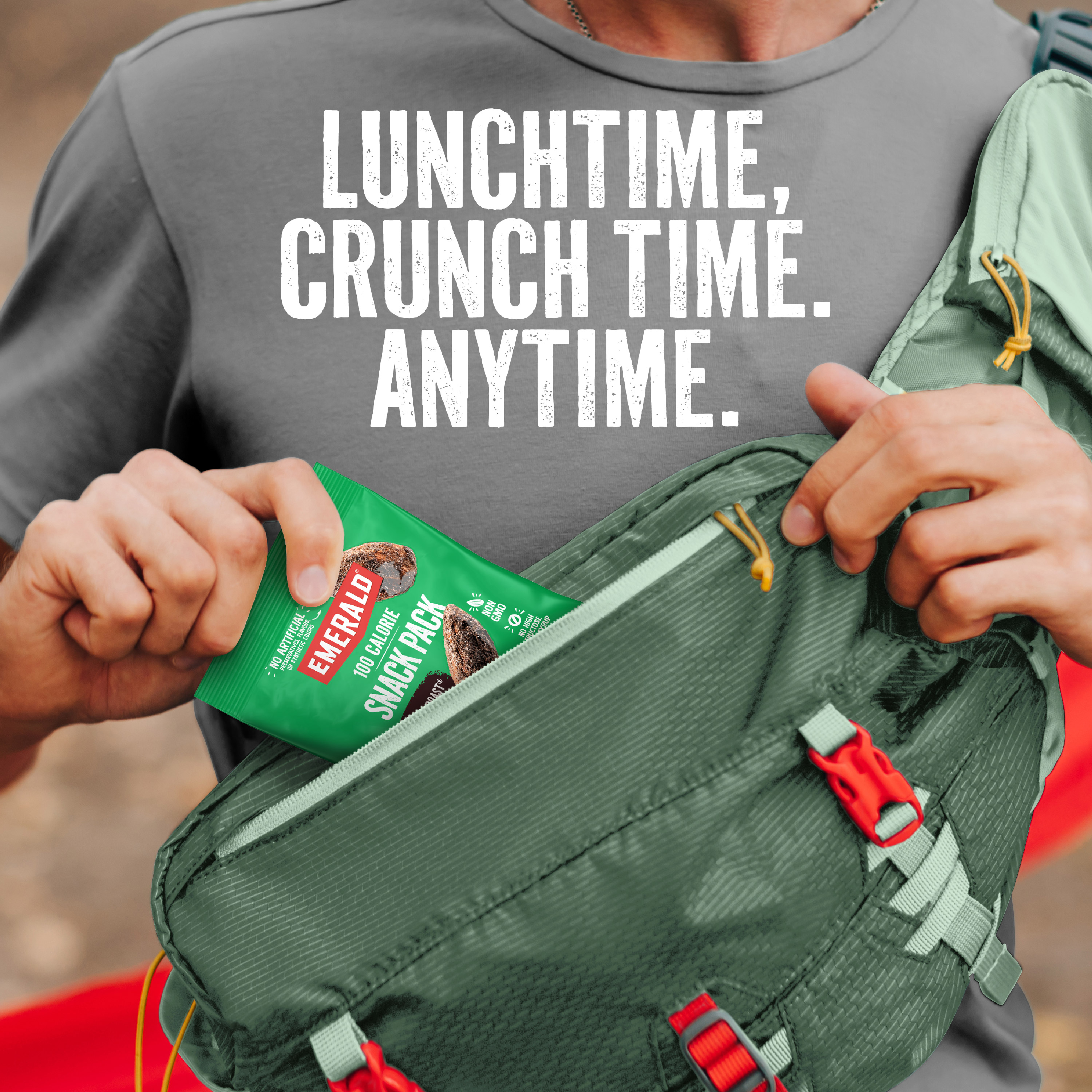 A person wearing a gray shirt is pulling a pack of Emerald nuts out of a green fanny pack. The text reads, Lunchtime, Crunch Time, Anytime.